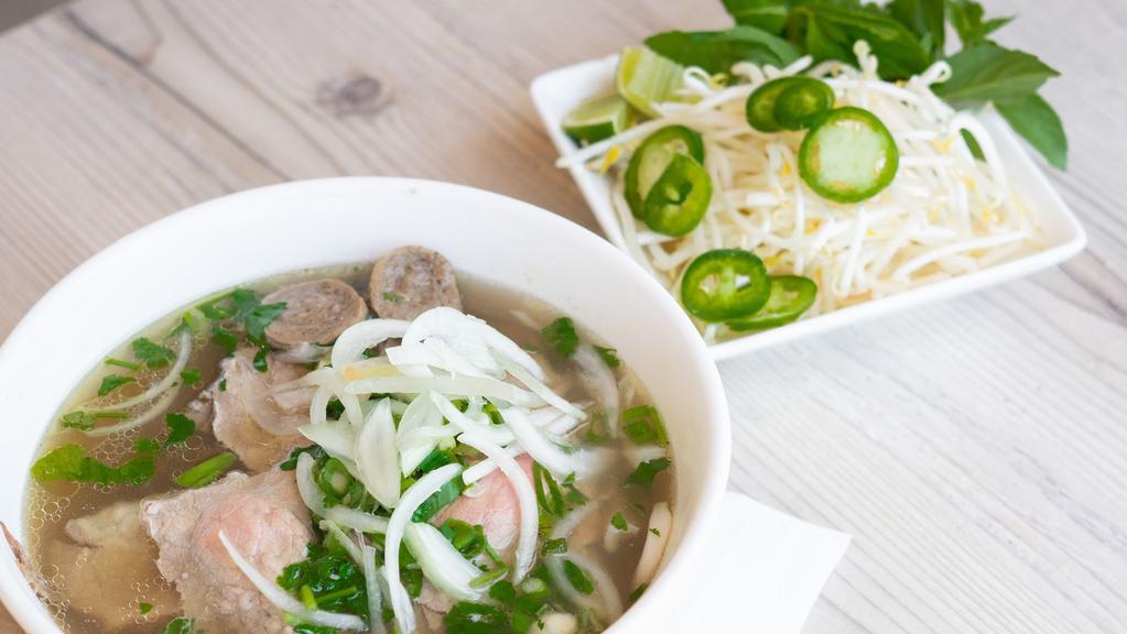 Pho Combo | Phở Dặc Biệt · Rare steak, well done brisket, tendon, tripe, beef ball served with house beef broth and thin rice noodles topped with cilantro, sliced onions, and green onions. Bean sprouts, basil, lime and jalapenos on the side.