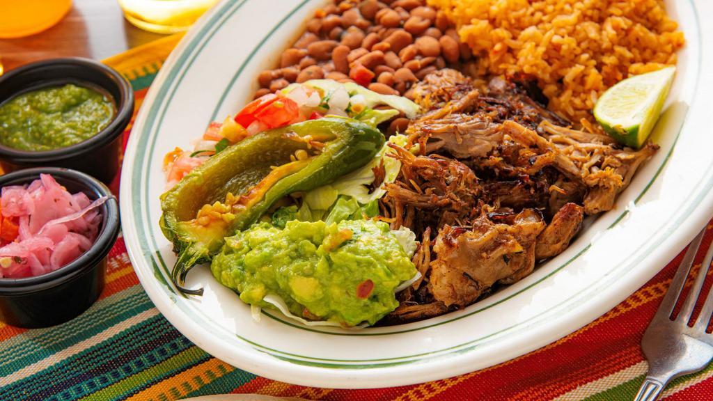 Carnitas · Traditional pork carnitas served with guacamole, pico de gallo, rice, whole beans, a roasted jalapeño, and tortillas.