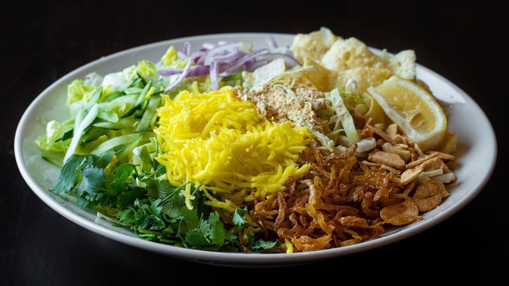 Mango Salad · Gluten-free, Pickled mango with fried garlic, cabbage, red onions, cucumber, cilantro, yellow bean powder and fried onions, onion oil and dried shrimp powder on a bed of romaine. Vegetarian Option Available