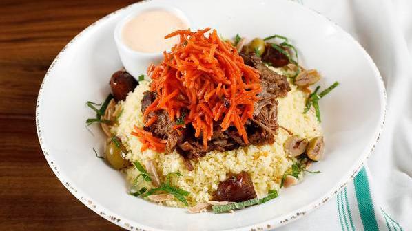 Lamb Tagine Bowl · Served over preserved lemon couscous with a carrot and dried fig slaw, topped with toasted almonds and a harissa yogurt sauce