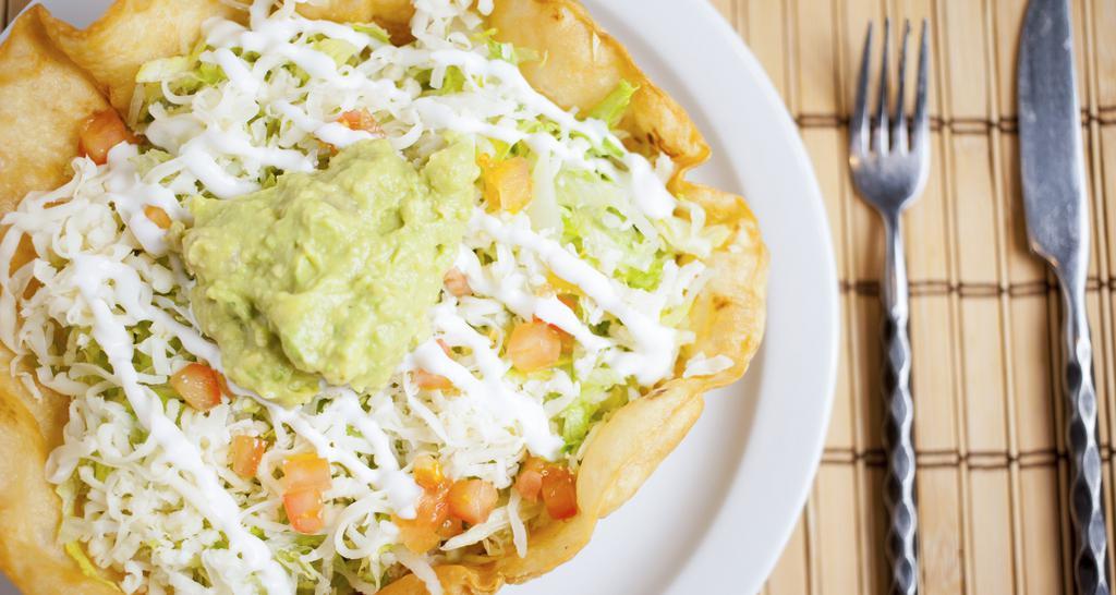 Tostada Suprema · A crispy flour shell covered with beans, meat topped with shredded lettuce, cheese, sliced tomatoes, guacamole, and sour cream.