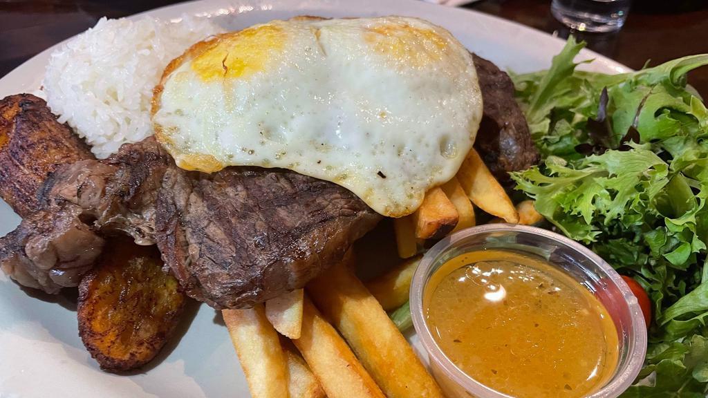 Bistec a lo Pobre · Gluten-free. Grilled ribeye steak (USDA), fried egg, French fries & fried plantains, served with rice & salad.