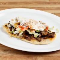 Huarache · Handmade corn-based long beans and cheese filled tortilla topped with meat, beans, sour crea...
