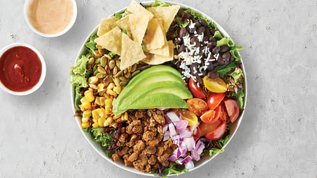 Super Taco Salad · Plant based protein sauteed with onions on a bed of spring mix, avocado, red onions, roasted pumpkin seeds, black beans with Cotija cheese, heirloom clam shell tomatoes, corn chips, roasted corn, with sides of chipotle ranch dressing and red chili salsa