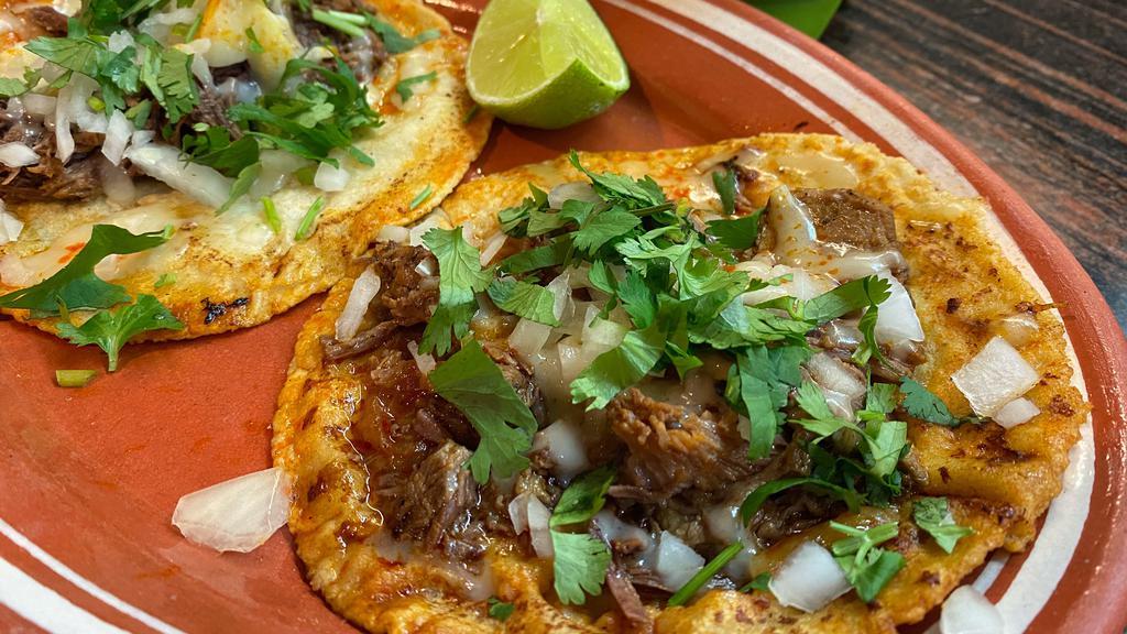 Birria Tacos · Beef slowly simmered in a house-made red broth, served with melted Cheese, Onions, Cilantro, and a side of Consomé.