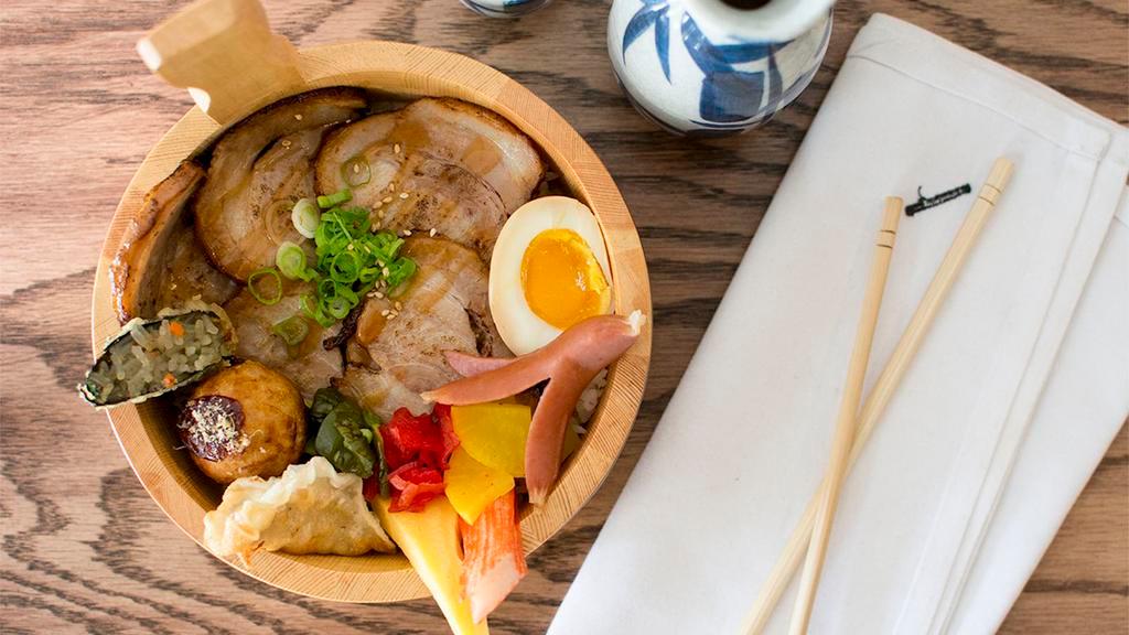 Chashu Don · Japanese rice bowl topped with seared pork belly, with sides of soft boiled egg, gyoza, takoyaki, tsukemono, and green onion.