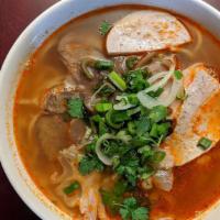 B11. Hue Spicy Noodle Soup · Bún Bò Huế.  Served with pork, beef tendon, brisket, Vietnamese ham, and side of bean spr...