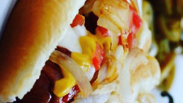 Loaded Bacon Wrapped Hot Dog · Bacon wrapped dog topped with 
 meat of your choice, fresh tomatoes, raw onion, mayo, ketchup, mustard and our signature orange sauce. Served with a side of grilled onions and a grilled jalapeno pepper.