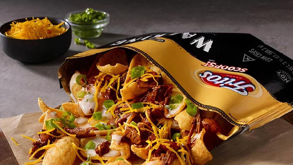 Brisket Chili Walking Taco · Texas-style brisket chili over a bed of Fritos, topped with creamy Poblano Queso, shredded cheddar cheese, and green onions. Built in a walking taco bag for enjoyment at the table or on the go.