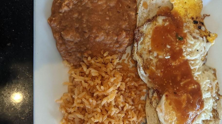 Huevos Rancheros · Eggs over easy served over corn tortillas, topped with a red sauce, and cheese, alongside rice, and refried beans.