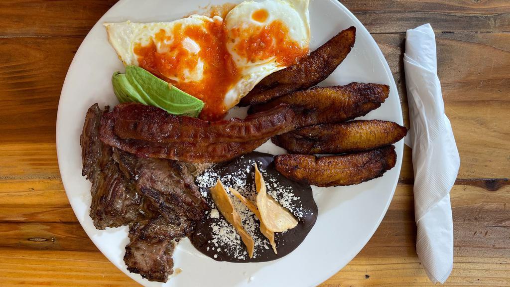 Desayuno  Guatemalteco  · Small Slice of meat (carne asada), crispy bacon, 2 sunny side eggs with tomatoes sauce on the side, black beans (casamiento or refried beans) with cheese and chips on top,  fried plantains, and slices of avocado. + two tortillas