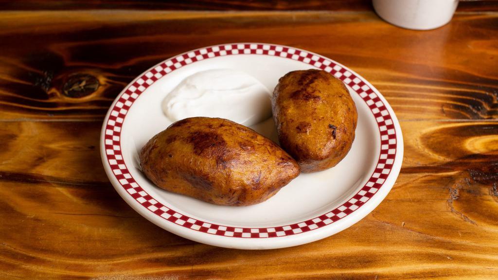 2 rellenitos de frijol con crema y azúcar · A small ball of fried plantains with black beans inside topped with sugar and sour cream on the side.