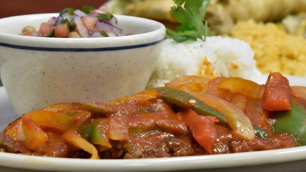 Bistec encebollado · Bistec marinated and cooked with fresh onions. Served with rice, refried beans, and tortillas.