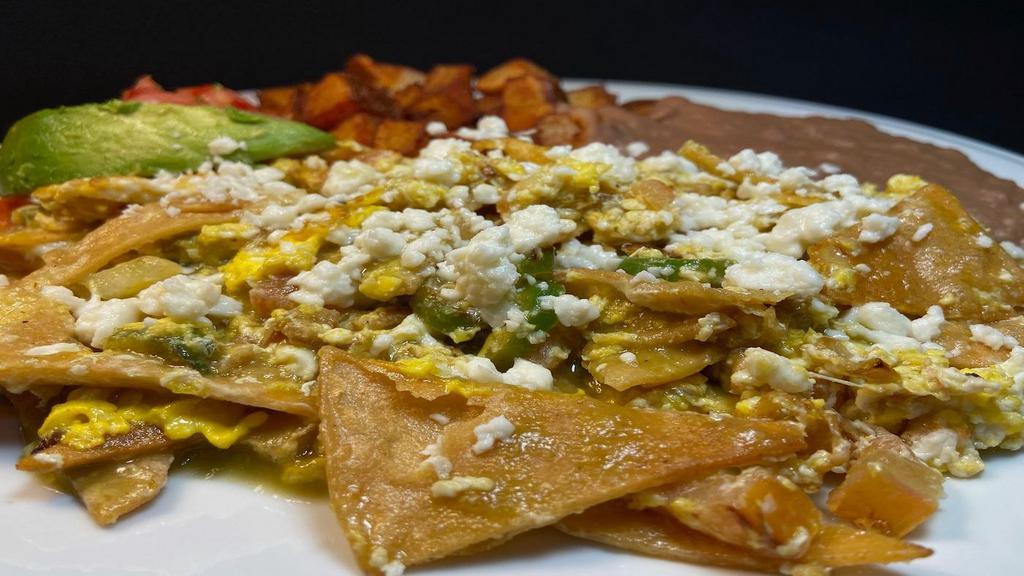 Chilaquiles Plate · Fried tortilla strips, 2 scrambled eggs, serranos, onions, tomatoes, tomatillo sauce and mexican cheese, served with refried beans, grilled potatoes, salsa fresca & avocado slice.