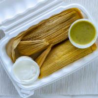 Tamales De Elote · Two sweet corn homemade tamales topped with a fresh tomatillo sauce and sour cream.