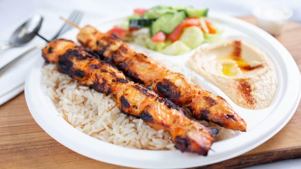Chicken Kabob Plate · Chicken kabob plate served with side of rice, hummus, greek salad, and fresh pita bread along with grilled onions and tomatoes on top.