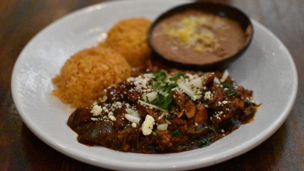 Tradicional Mole Poblano · Shredded chicken simmered in our house-made fifteen ingredient mole sauce topped with cilantro, onions, and queso cotija. Served with beans, rice and tortillas.  Contains peanuts.