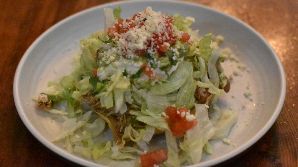 Tostada · Your choice of meat, refried beans, lettuce, tomatoes, queso cotija, Mexican crema and guacamole piled high on a crispy corn tortilla shell.