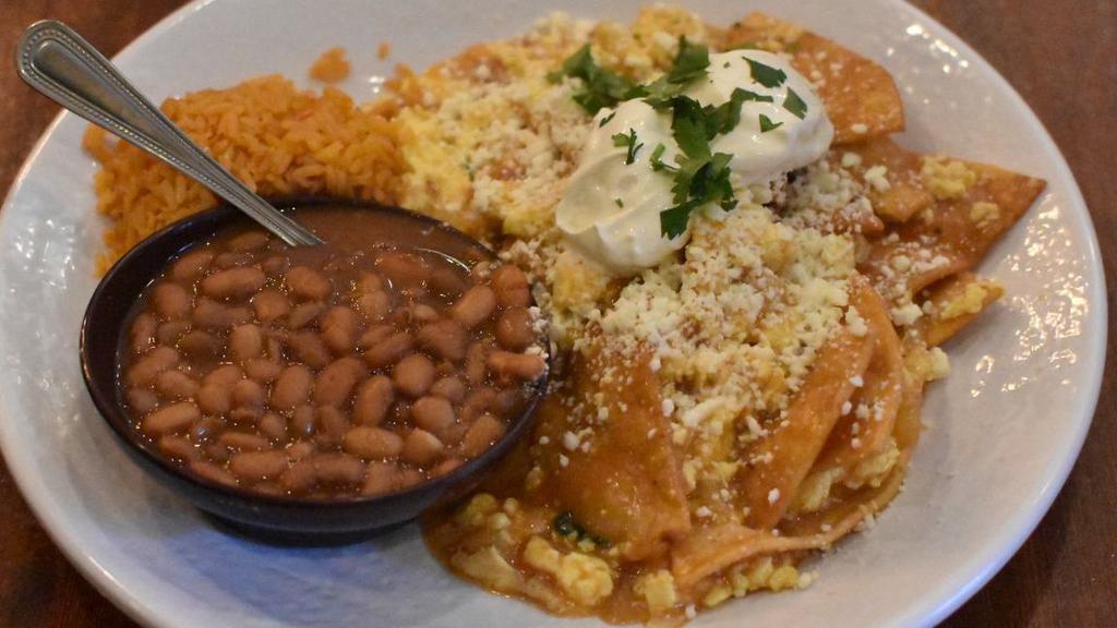 Chilaquiles Breakfast · Crispy corn tortilla chips and scrambled eggs in guajillo and ranchera salsas, with Mexican crema, queso cotija, and cilantro. Served with beans and rice.