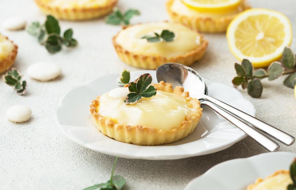 Lemon Curd · A buttery short dough tart shell filled with lemon curd, sprinkled with granulated sugar topping, torched until caramelized, and finished with a light dusting of confectionery sugar.