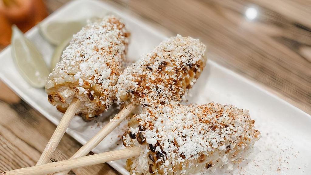 Elote · Grilled Mexican style street corn rolled in spices, topped with queso fresco, Cotija, and lime.