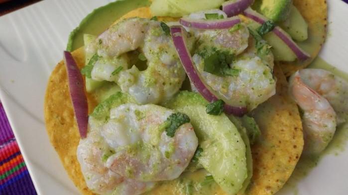 Aguachile Tostada · Lime fermented shrimp, sliced onion, sliced cucumber, sliced tomato, avocado on top, sprinkled dried chilies (Very Spicy). 
Camaron curtido, cebolla, pepino, tomate, aguacate, y chile rojo en polvo.