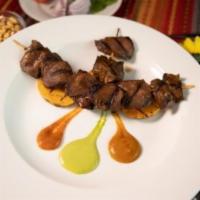 Anticuchos de Corazon · Beef heart skewers marinated in ají panca, served with grilled potato and Peruvian Chile pep...
