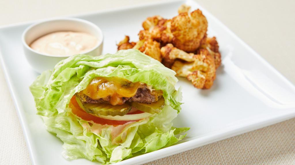 Paleo Lettuce Wrapped Burger · Lettuce wrapped fresh grilled seasoned beef patty, tomato, onion and pickles. Served with fried cauliflower and almond bitchin sauce. Gluten-free. Dairy-free.