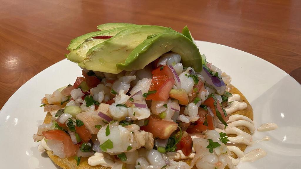 Ceviche Tostada · Shrimp, fresh lime juice, avocado slice, tomatoes, onions, cucumber, jalapeños, cilantro, mayonnaise on top of corn tostada.