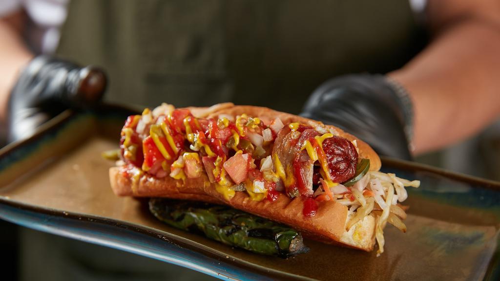 The MVP Sonora Dog · Applewood Bacon-wrapped hot dog on griddled bun. griddled onions & peppers, house curtido, house pico, mayo, mustard, Tapatio ketchup.