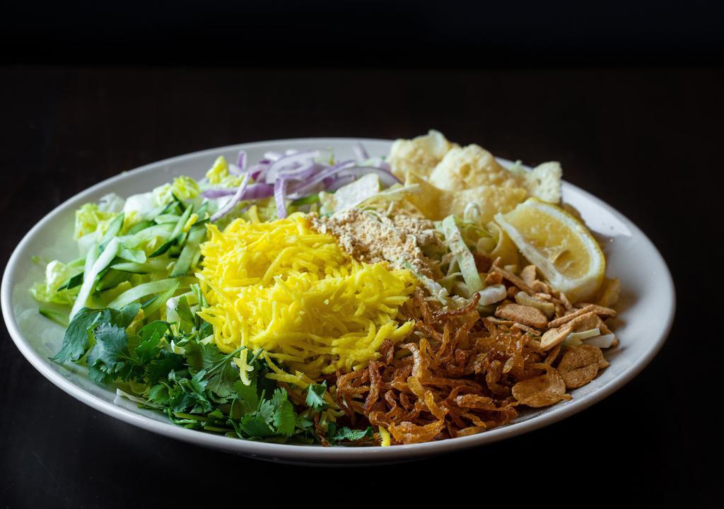 Mango Salad · Pickled mango with fried garlic, cabbage, red onions, cucumber, cilantro, yellow bean powder and fried onions, and onion oil on a bed of romaine lettuce and a fresh squeeze of lemon.