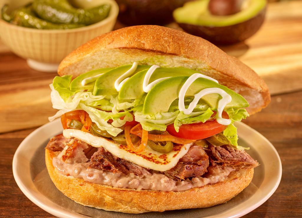 Torta Al Gusto · Stuffed with refried beans, mayonnaise, sour cream, avocado, lettuce, tomatoes, caramelized onions, pickled jalapenos, and panela cheese.