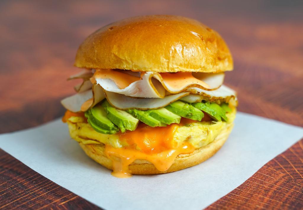 Brioche, Smoked Turkey, Avocado, Egg, & Cheddar Sandwich · 2 scrambled eggs, melted Cheddar cheese, sliced smoked turkey, avocado, and Sriracha aioli on a warm brioche bun.