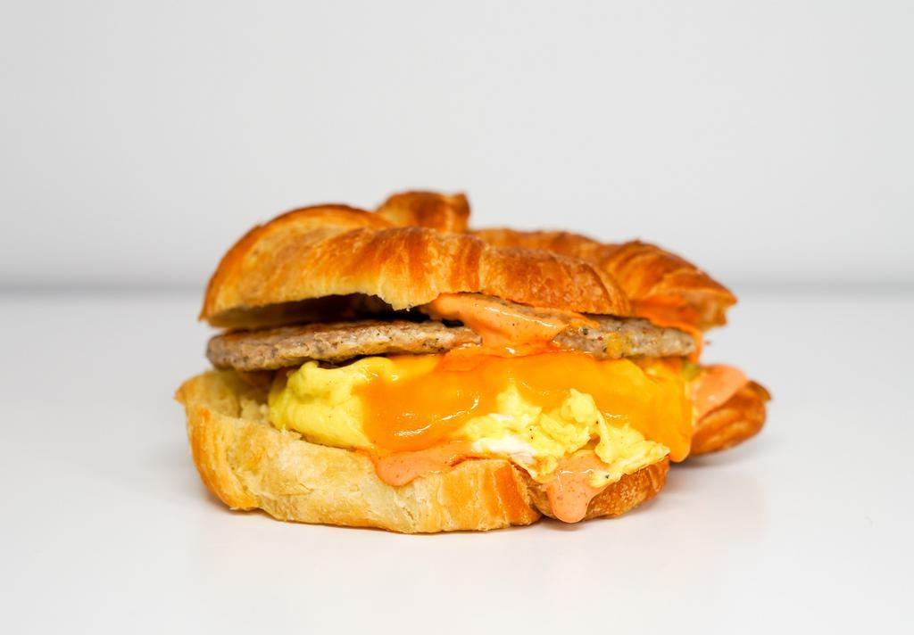 Croissant, Sausage, Egg, & Cheddar Sandwich · 2 scrambled eggs, melted Cheddar cheese, breakfast sausage, and Sriracha aioli on a warm croissant.