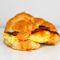 Croissant Bacon, Egg And Cheddar Sandwich · 2 scrambled eggs, melted Cheddar cheese, smoked bacon, and Sriracha aioli on a  warm croissant