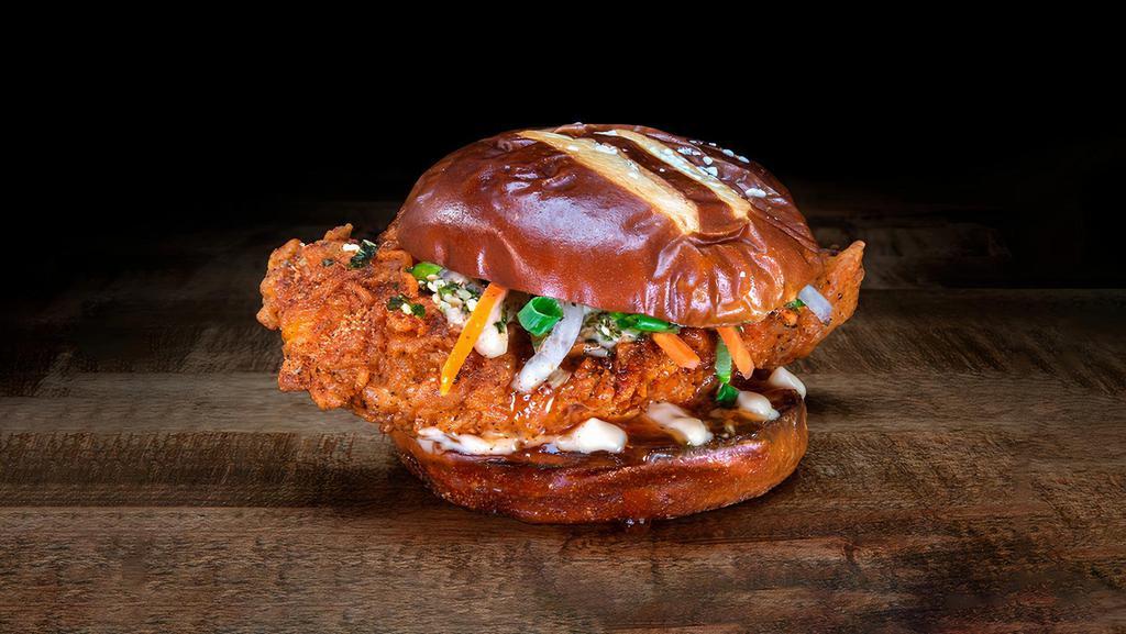 Honolulu Hot Chicken · Chef Logan Sandoval’s Honolulu Hot Chicken features a crispy hot chicken tender, topped with pickled carrots and onions, scallions and wasabi furikake, drizzled with miso aioli, sweet chili sauce, and served on a King’s Hawaiian pretzel hamburger bun.