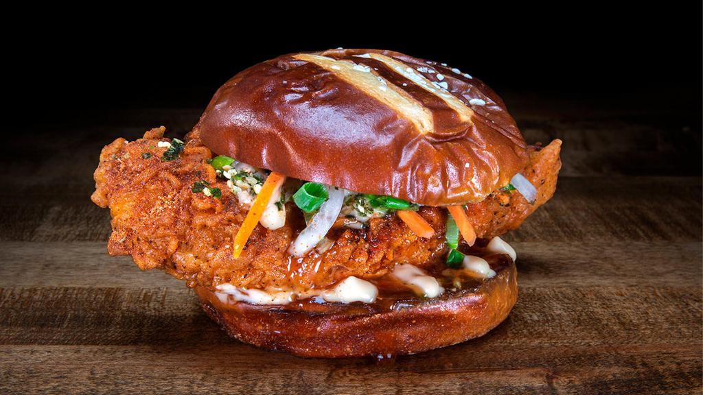 Honolulu Hot Chicken · Chef Logan Sandoval’s Honolulu Hot Chicken features a crispy hot chicken tender, topped with pickled carrots and onions, scallions and wasabi furikake, drizzled with miso aioli, sweet chili sauce, and served on a King’s Hawaiian pretzel hamburger bun.