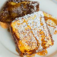 French Toast · Three slices of thick, egg-washed brioche bread with syrup and powdered sugar.