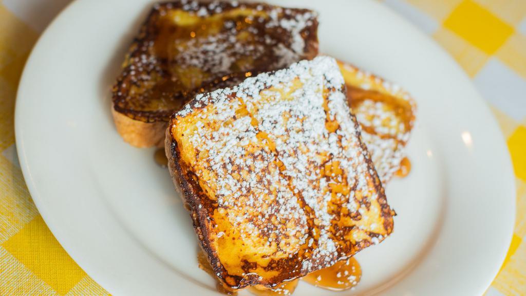 French Toast · Three slices of thick, egg-washed brioche bread with syrup and powdered sugar.