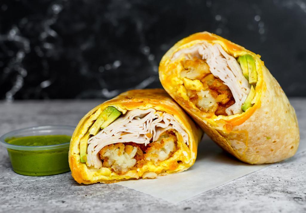 Smoked Turkey, Avocado, Egg, & Cheddar Breakfast Burrito · 3 fresh cracked, cage-free scrambled eggs, melted Cheddar cheese, sliced smoked deli turkey, fresh avocado, and crispy potato tots wrapped in a toasted 12” flour tortilla. Comes with avocado salsa verde side.