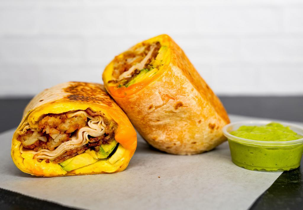 Turkey Bacon, Turkey, Avocado, Egg, & Cheddar Breakfast Burrito · 3 fresh cracked, cage-free scrambled eggs, melted Cheddar cheese, crispy turkey bacon, sliced smoked deli turkey, fresh avocado, and crispy potato tots wrapped in a toasted 12” flour tortilla. Comes with avocado salsa verde side.