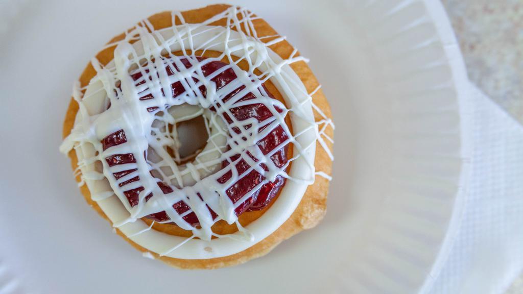 White Chocolate Raspberry Cheesecake · Raised yeast donut topped with raspberry, cream cheese icing, and white chocolate drizzle