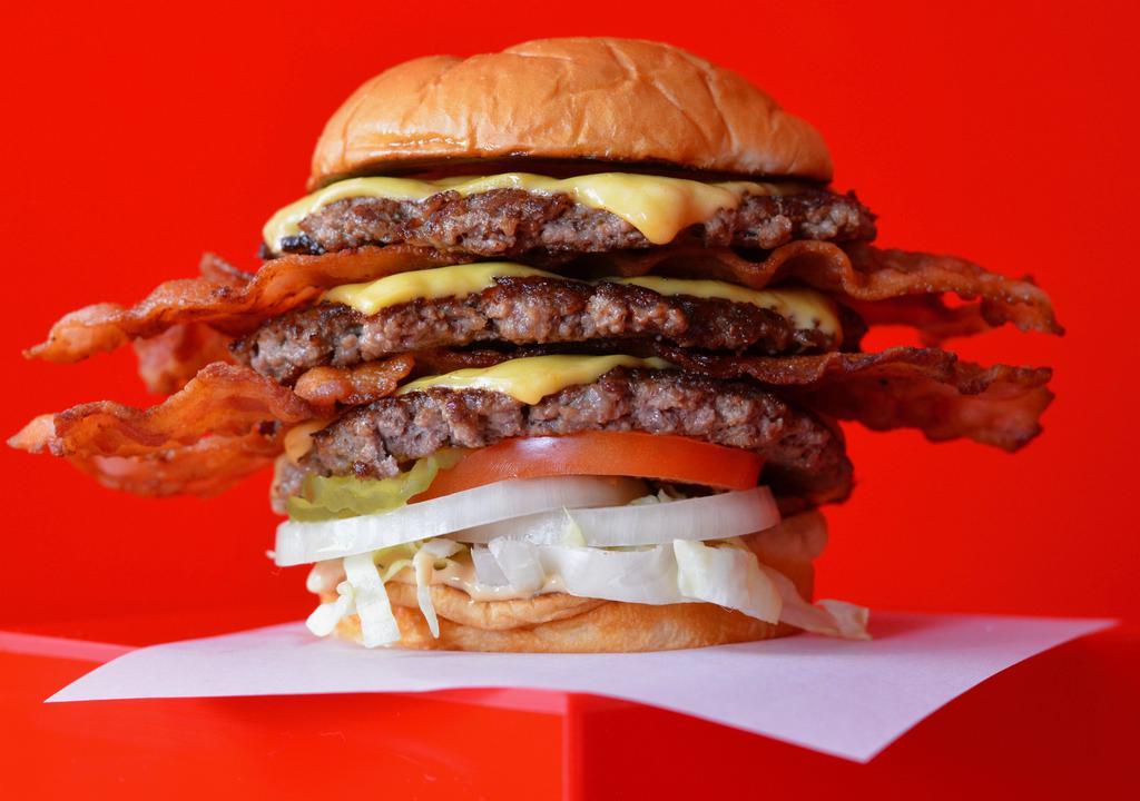 Super Smash Triple Cheeseburger · Three juicy grilled beef burger patties each smashed to perfection on a toasted potato bun with American cheese, double stacks of smoked bacon, fresh lettuce, sliced tomato, pickles, onion and Super Smash sauce.