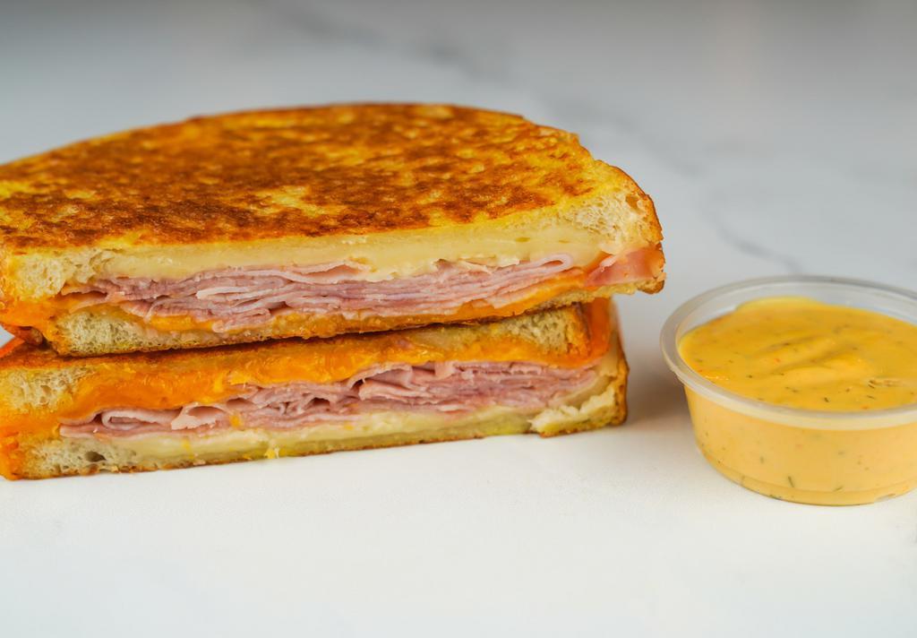 Smoked Ham & Cheese Monte Cristo · Smoked ham, Cheddar, Swiss, and Parmesan cheeses melted between egg dipped, griddled sourdough bread. Served with a side of Spicy Honey Mustard Aioli.