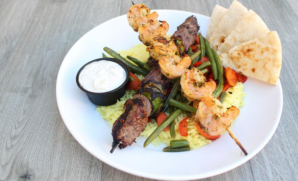Surf & Turf Plate · Grilled shrimp skewer and steak skewer served on a bed of seasoned basmati rice with roasted vegetables, choice of hummus or tzatziki, and warm pita.
