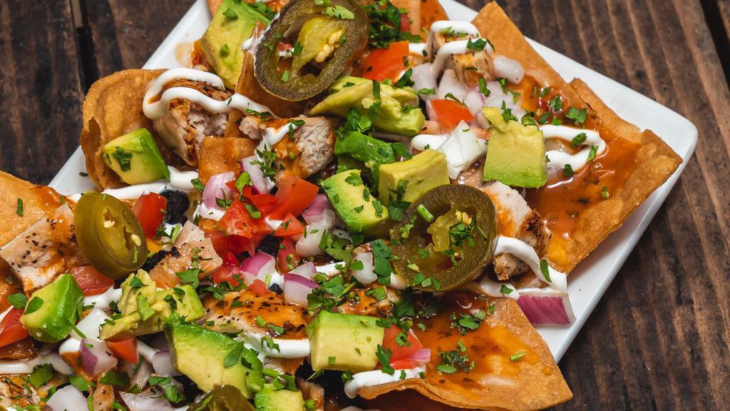 Grilled Chicken Nachos · Black beans, avocado, tomatoes, cilantro, red onions, cheese blend, sliced jalapenos, chipotle sauce, and crema.