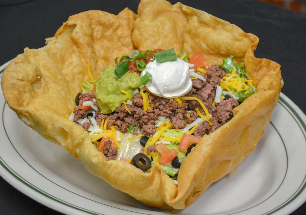 Taco Salad · Crisp mixed greens tossed with our chipotle ranch dressing, topped with seasoned ground beef, black beans, tomatoes, olives, cheddar and mozzarella cheese, guacamole, salsa, sour cream, green onions, and served in a large tortilla shell.