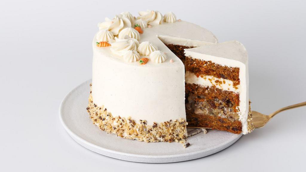 Slice Carrot Cake · Rich carrot cake full of spices, walnuts and raisins, layered with walnut-caramel filling and cream cheese, decorated with vanilla buttercream frosting and toasted walnuts.
