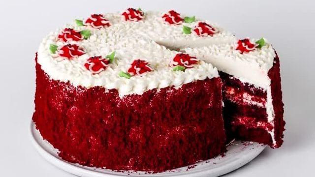 Slice Red Velvet Cake · Rich and red buttermilk cake with layers of cream cheese filling and frosting, decorated with buttercream poppies and toasted red velvet cake crumbs.
