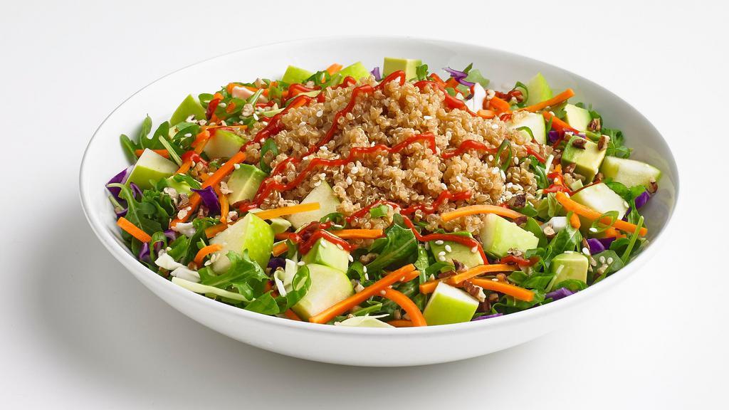 Quinoa Bowl · A quinoa rice blend on top of fresh spinach tossed in vinaigrette dressing with cabbage, shredded carrots, toasted pecans, sesame seeds, apples, and avocado. Garnished with green onion and Sriracha sauce.